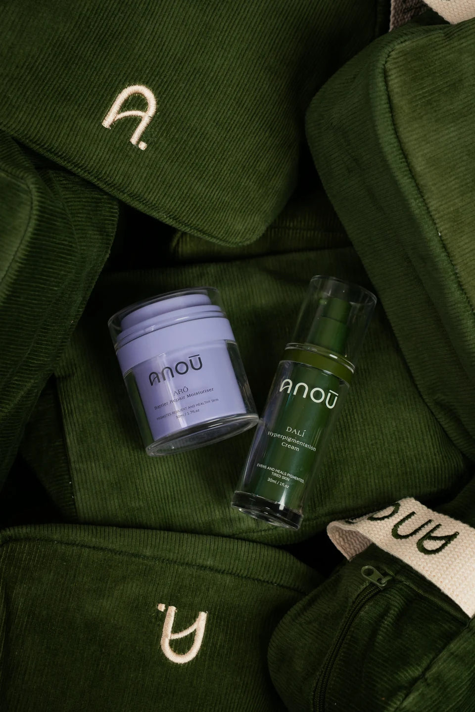 Arō moisturiser and Dalí cream resting on olive-green corduroy Carryall pouches.
