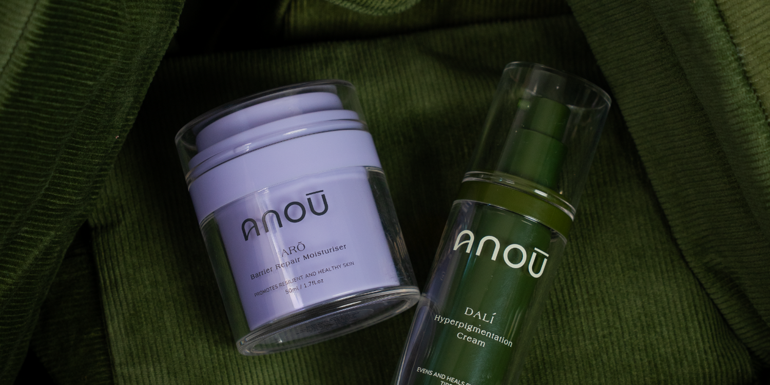 Two skincare products from the brand 'ANOU' on a green fabric background