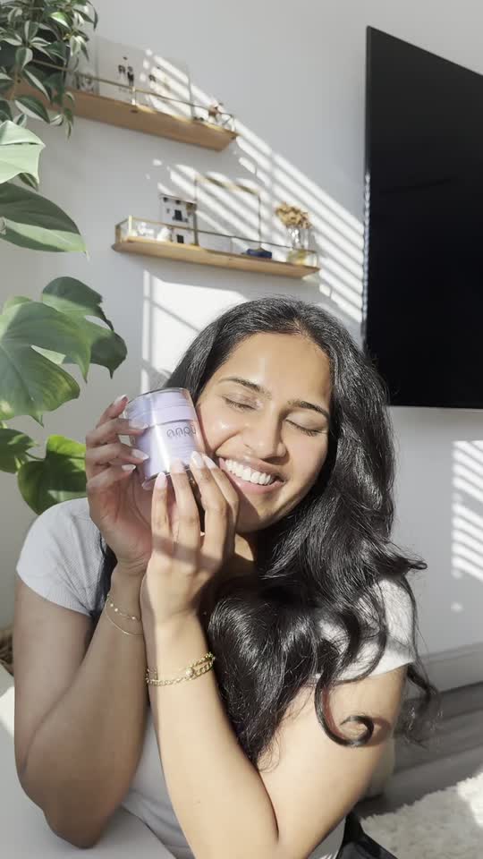 Video still of a smiling woman holding Arō beside her cheek in a sunlit room.