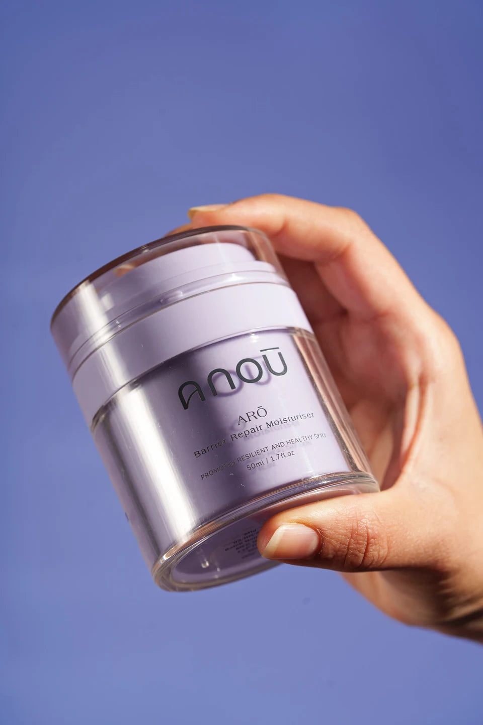 A hand holding the lilac Arō moisturiser jar against a lilac background.